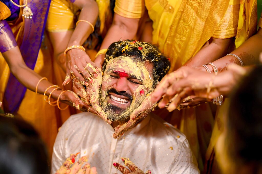 The Telugu Groom is celebrating haldi occassion, his friends rubs his face with haldi captured by Framesflow photography in Hyderabad